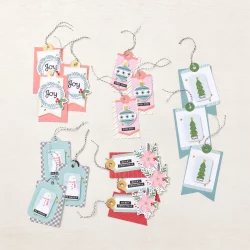 Image shows three each of five different tags you can make with the Festive Tags Kit from Stampin'Up. The theme is cartoon/graphic style images of trees, snowmen, flowers and wreaths.  Main colors are pink dark pink, light blue, dark blue & green.  